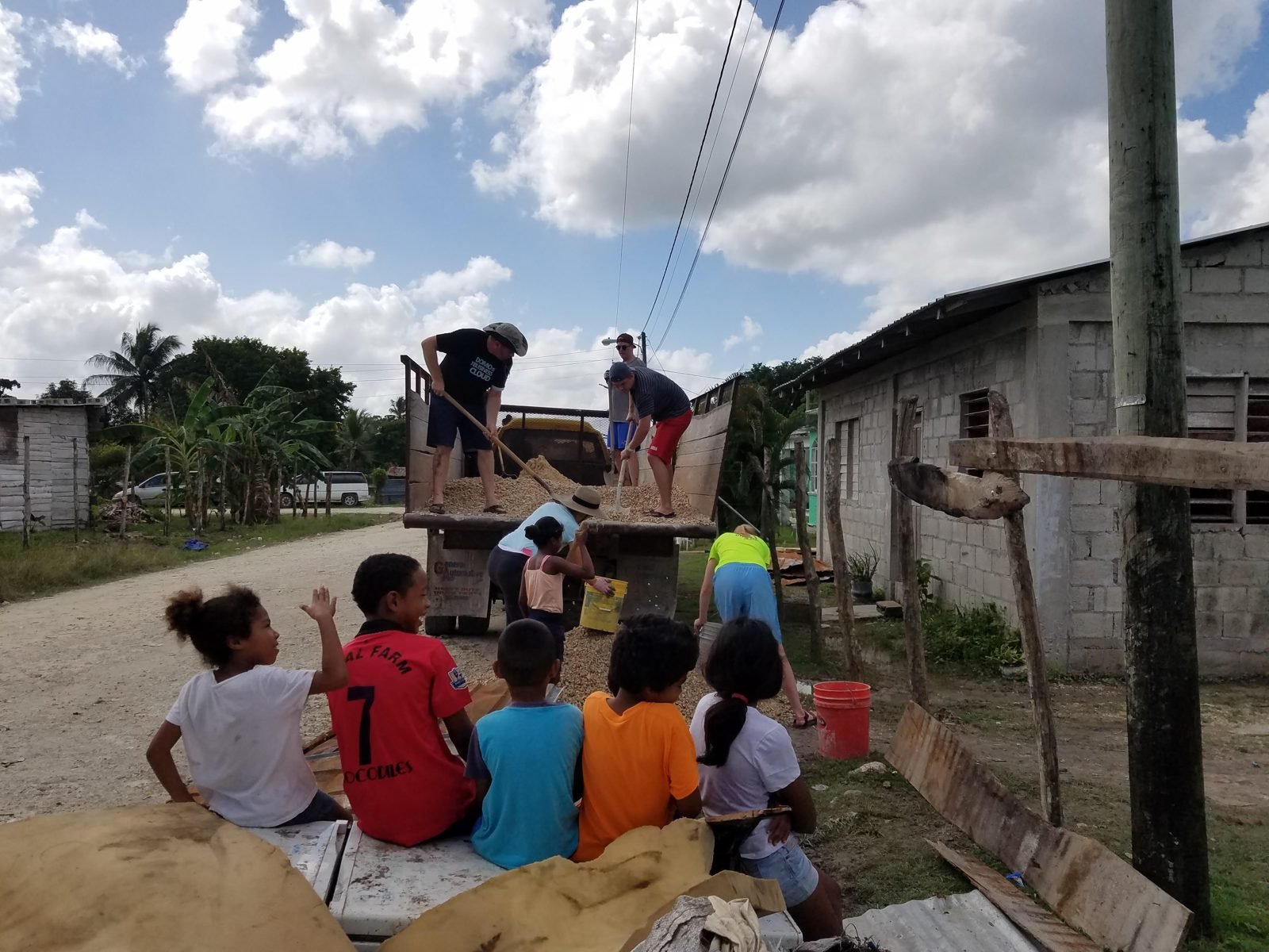 Local children sitting on a truck watching volunteers unload building materials in Belize.